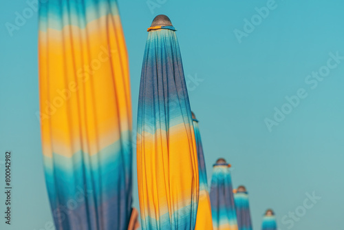 Folded colorful beach umbrella parasols on Adriatic sea coast in sunny summer morning, holiday and vacation background with copy space
