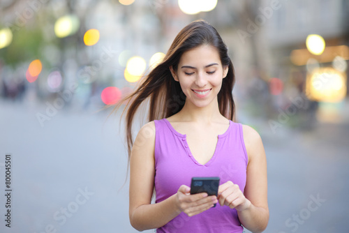 Happy woman walking using smart phone in the street