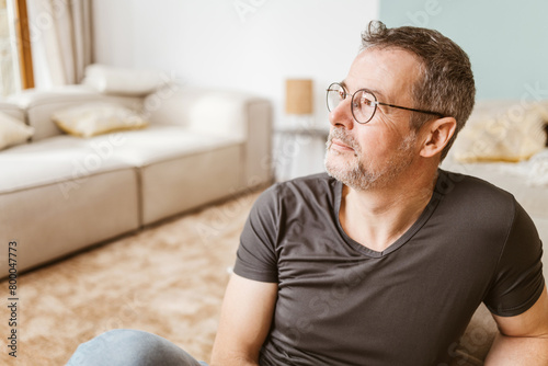 Pensive middle-aged man sitting on living room floor photo