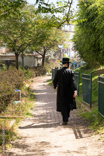 Religious jew in a black frock coat and black hat walks through a green park (179)