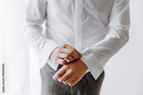 A man in a white shirt is adjusting his shirt sleeves. Concept of formality and attention to detail, as the man takes care to ensure his shirt is properly tucked in and his sleeves are neatly folded