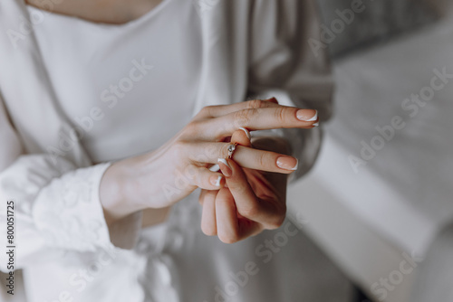A woman is holding a ring in her hand. She is wearing a white gown and has her hands clasped together
