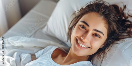Close-up of a joyful young woman smiling while relaxing in a comfortable and bright bedroom environment. © tashechka