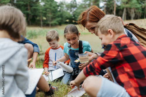 Young students analyzing water quality, ph level with indicator strips during biology field teaching class. Female teacher during outdoor active education.