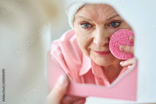 Senior woman applying moisturizer using face pad photo