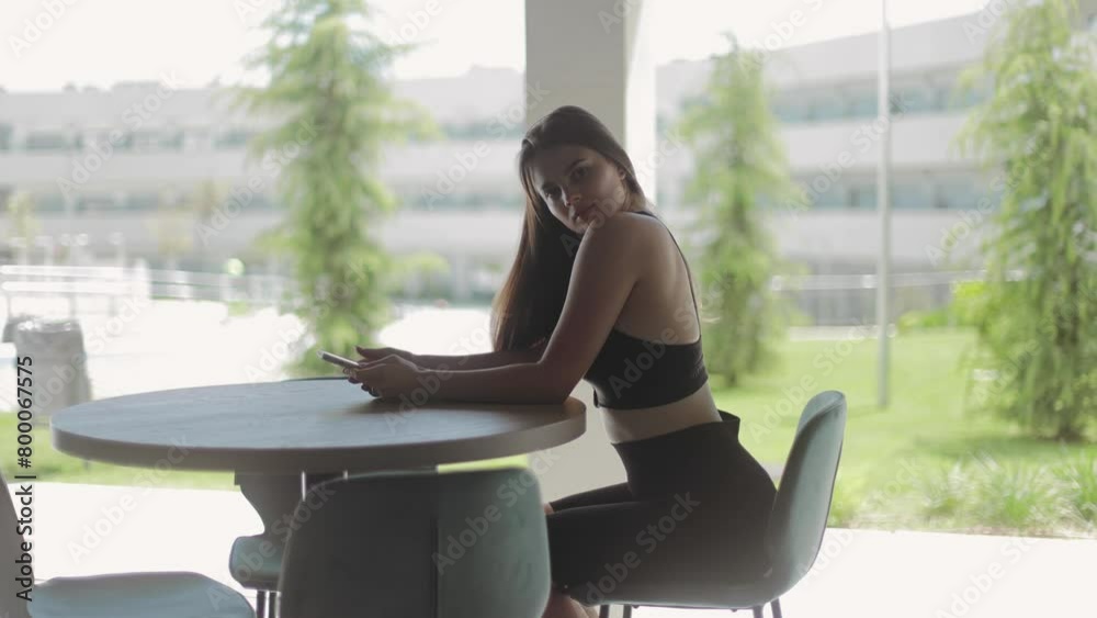 A beautiful young girl sits at a table in beautiful daylight and poses looking at the camera, sports girl, fitness girl, sports, casual, model, modeling, energy, body, gym, residential complex, wealth A beautiful young girl sits at a table in beautiful daylight and poses looking at the camera, sports girl, fitness girl, sports, casual, model, modeling, energy, body, gym, residential complex, wealth