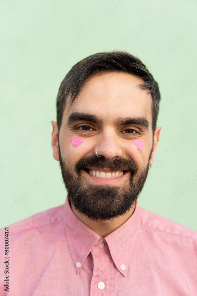 Happy man with pink heart shape stickers on cheeks against mint green background Happy man with pink heart shape stickers on cheeks against mint green background
