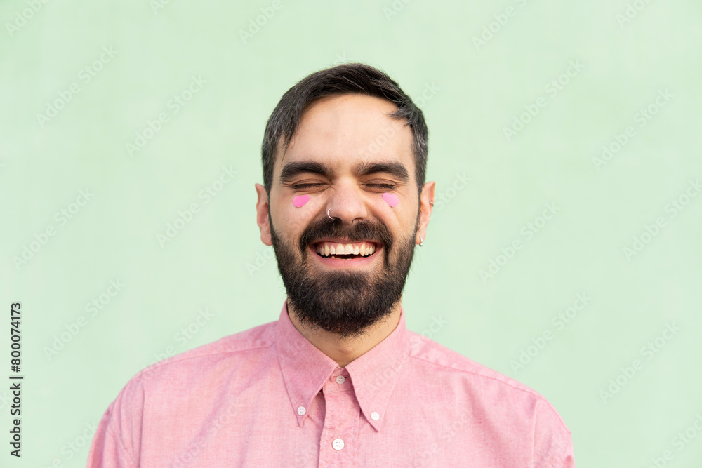 Cheerful man with pink heart shape stickers on cheeks against mint green background Cheerful man with pink heart shape stickers on cheeks against mint green background