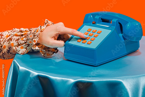 Woman dialing number on telephone against orange background
