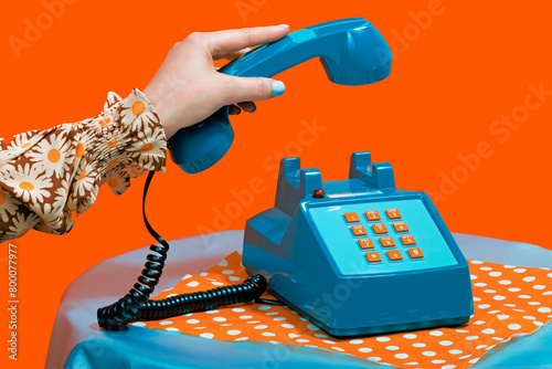 Hand of woman picking up telephone receiver against orange background photo