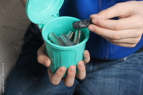 Young person contributing to recycling by throwing used batteries into a tiny bin, showcasing environmental responsibility and waste reduction. Eco-friendly image.