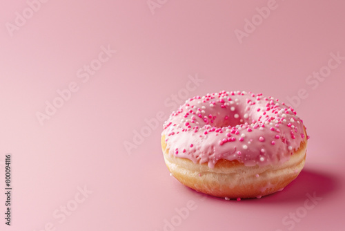 Freshly baked single donut with pink icing and white sprinkles, set on a soft pink background