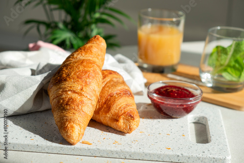 Fresh croissant for breakfast with jam on white board. Delicious celebratory breakfast in sunlight. Bakery or confectionery. Romantic morning meal.