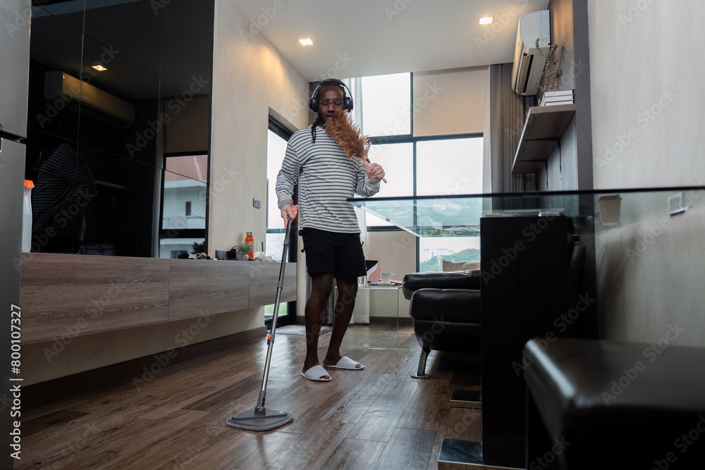 Funny African American is cleaning house doing housework cleaning floor with mop and listening to music in wireless headphones, African American man is dancing and singing Funny African American is cleaning house doing housework cleaning floor with mop and listening to music in wireless headphones, African American man is dancing and singing