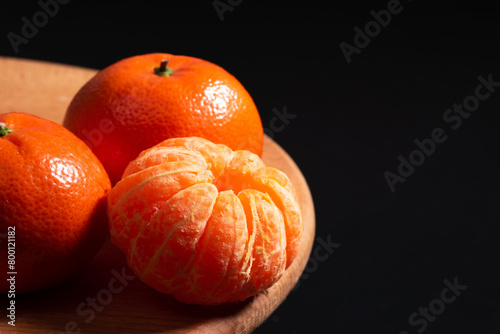 Three tangerines displayed on a wooden board against a black background