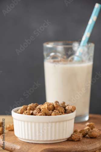 Close-up of white bowl with tiger nuts and glass of horchata out of focus, gray background, vertical, with copy space