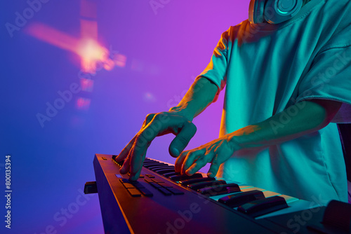 A vibrant DJ performance: a young man, eyes glued to the mixer, orchestrates the night's soundtrack against gradient pink purple background in neon light. Concept of music, performance, live concert