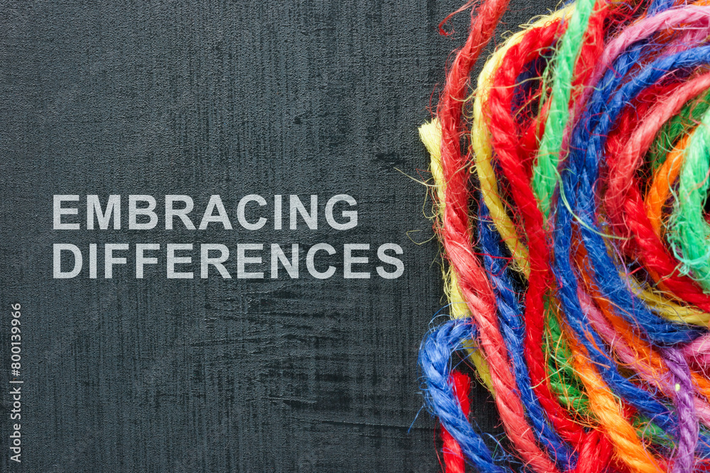 Obraz premium Words Embracing differences next to a ball of colored threads.
