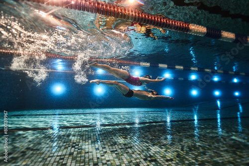 beautiful athletes swimmers guy and girl synchronously swim underwater in the pool on top of each other in dolphin style