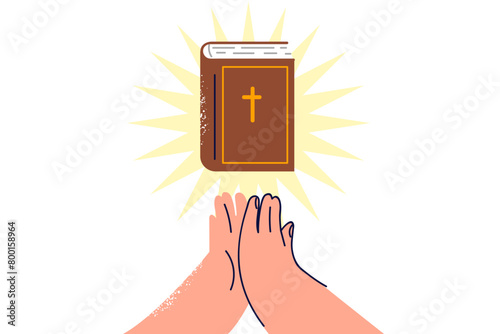 Bible with rays of light near hands of praying man who professes christian religion