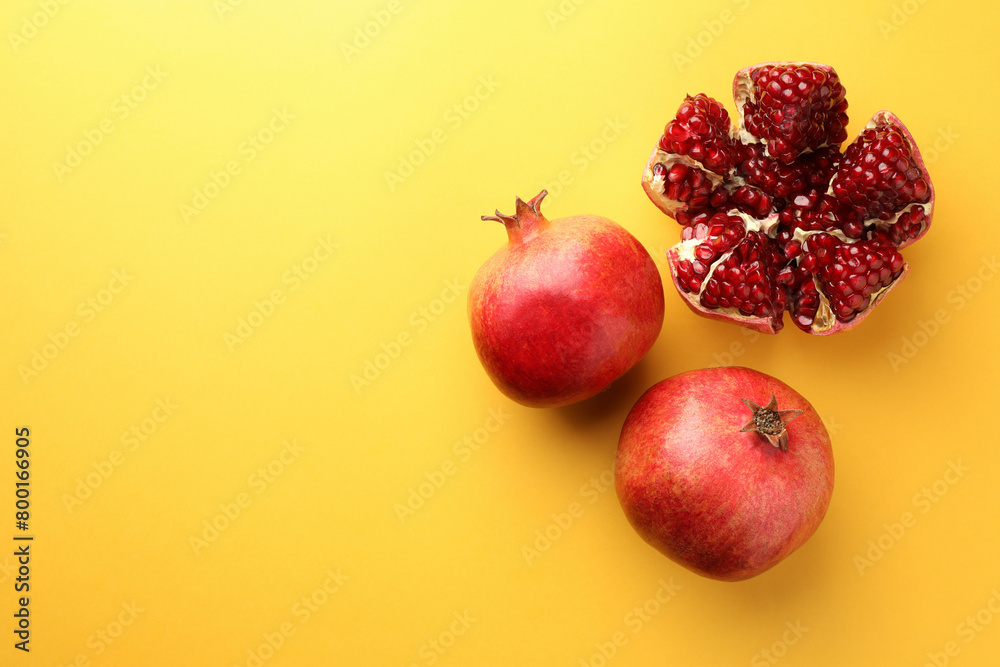 Whole and cut fresh pomegranates on yellow background, flat lay. Space for text Whole and cut fresh pomegranates on yellow background, flat lay. Space for text