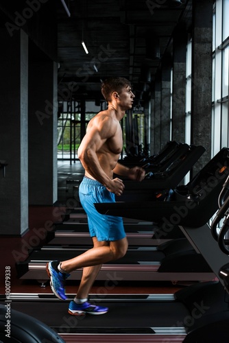 Side view full length young man sportswear running treadmill gym muscular young man blue shorts doing exercises motion blur
