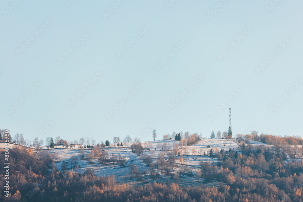 A majestic snow-covered hill rises with grace, its peak adorned by a towering radio tower under the wintry sky