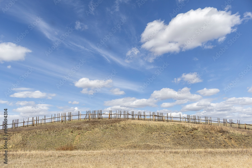 Rural scene of a broken weathered old wooden fence curving with the hilltop under a blue sky with white clouds.