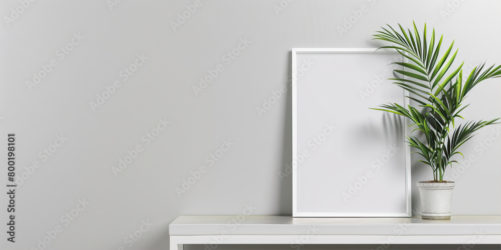 White empty frame on a background of a gray wall next to a plant
