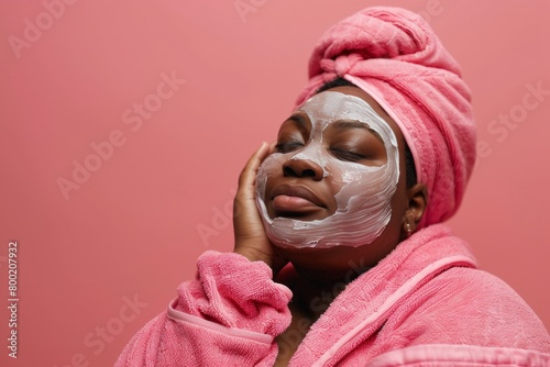 young plus size african female with towel on head applying face mask  isolated on plain background  skincare portrait of woman after shower