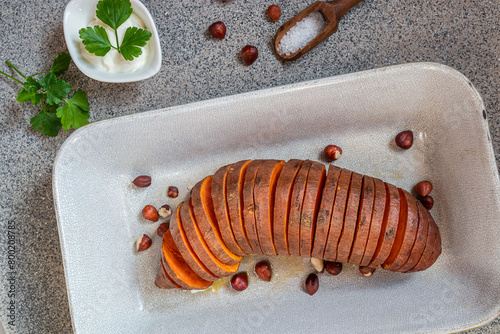 Roasted hasselback sweet potatoes with spices on a dark table close-up