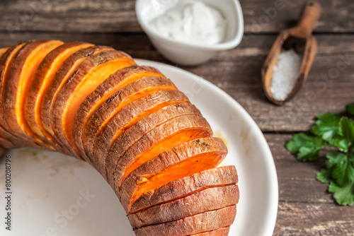 Roasted hasselback sweet potatoes with spices on a wooden table close-up
