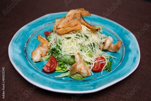 Fresh and tasty salad with greens, tomatoes, and shrimps on a blue plate