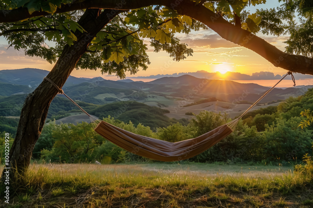 Naklejka premium Hammock suspended between trees with a view of rolling hills and sunset in tranquil countryside setting.
