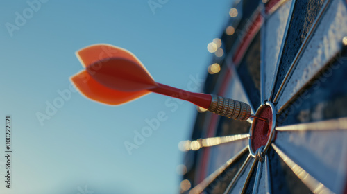 A close-up image capturing an orange dart precisely embedded in the bullseye of a classic dartboard with a clear sky background