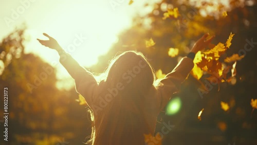 Young woman having positive good mood throwing fallen maple leaves in air in sunny autumn weather in park, back view. activity recreation entertainment in fall season, playing with foliage concept.