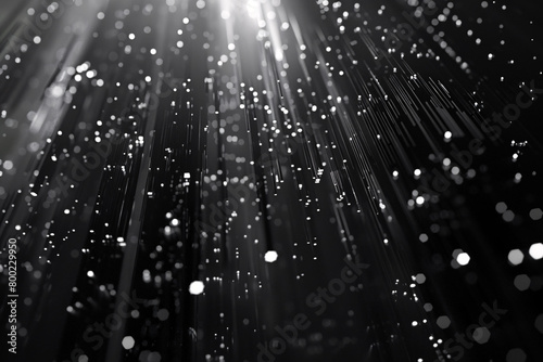 Abstract black and white image of vertical light rays interspersed with glowing particles against a dark backdrop