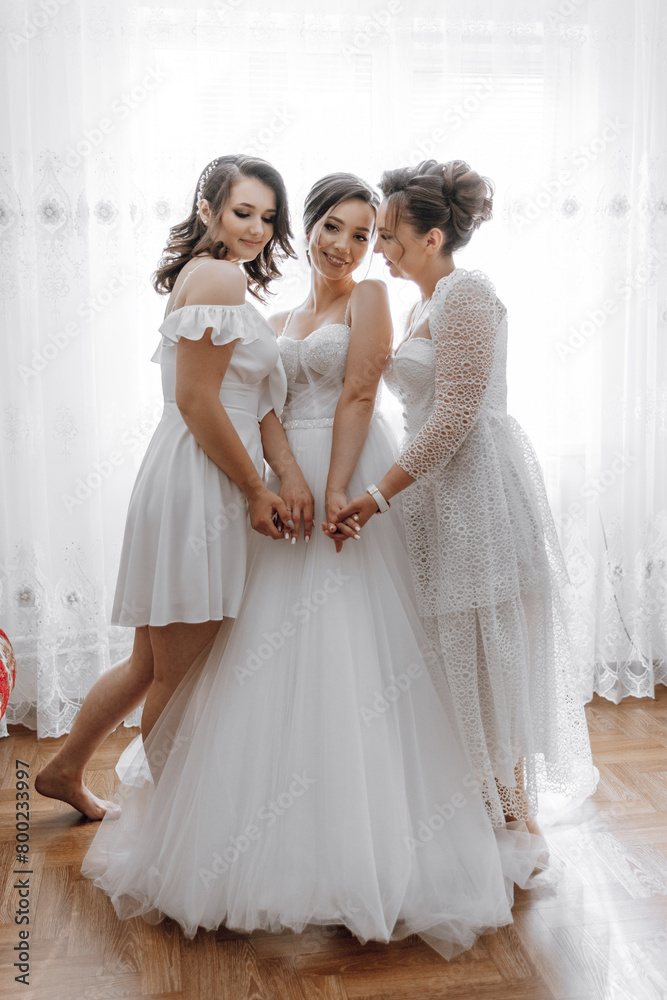 Three women are posing for a picture, with one of them wearing a wedding dress. The other two women are standing behind her, and they are all smiling. Scene is happy and celebratory Three women are posing for a picture, with one of them wearing a wedding dress. The other two women are standing behind her, and they are all smiling. Scene is happy and celebratory