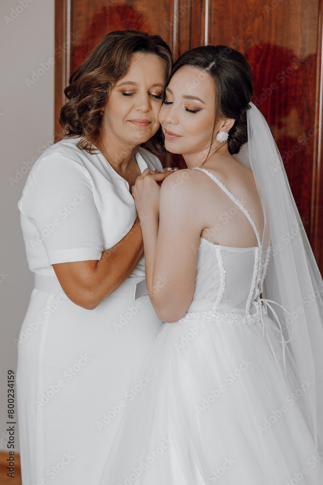 A bride and her mother are hugging each other. The bride is wearing a white dress and the mother is wearing a white dress as well A bride and her mother are hugging each other. The bride is wearing a white dress and the mother is wearing a white dress as well