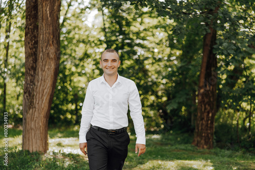 A man in a white shirt and black pants walks through a forest. He is smiling and he is enjoying his time in nature © Vasil