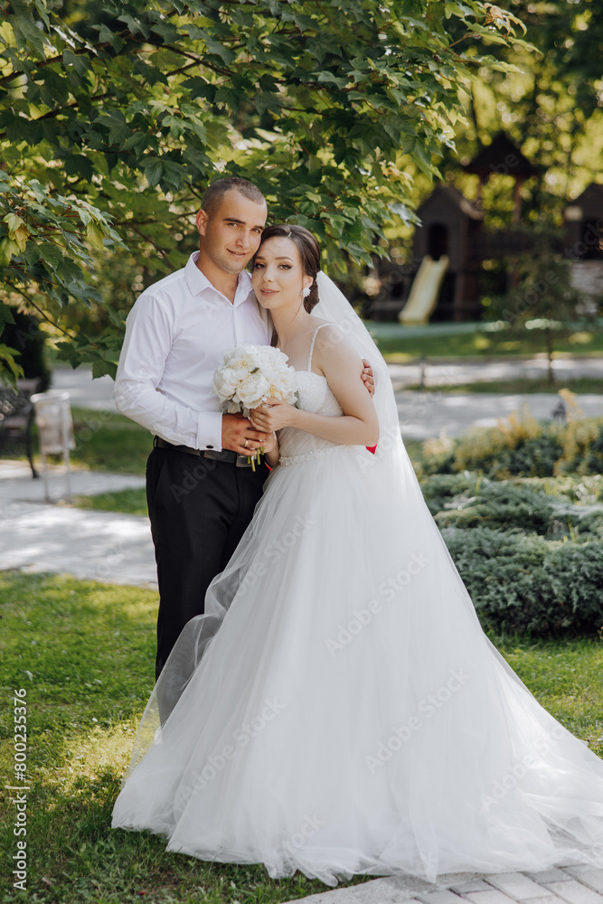 A bride and groom are posing for a picture in a park. The bride is holding a bouquet and the groom is holding her hand. Scene is happy and romantic A bride and groom are posing for a picture in a park. The bride is holding a bouquet and the groom is holding her hand. Scene is happy and romantic