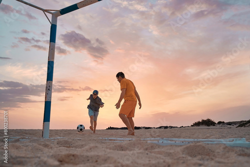Father and Son playing football, family fun outdoors players in soccer in dynamic action have fun playing football in the beach, summer day under sunlight.	