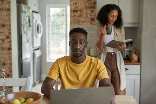 Young multiethnic couple doing different things during breakfast in kitchen