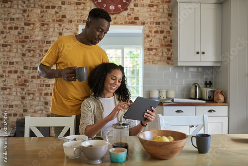 Smiling multiethnic couple using a tablet in their kitchen in the morning