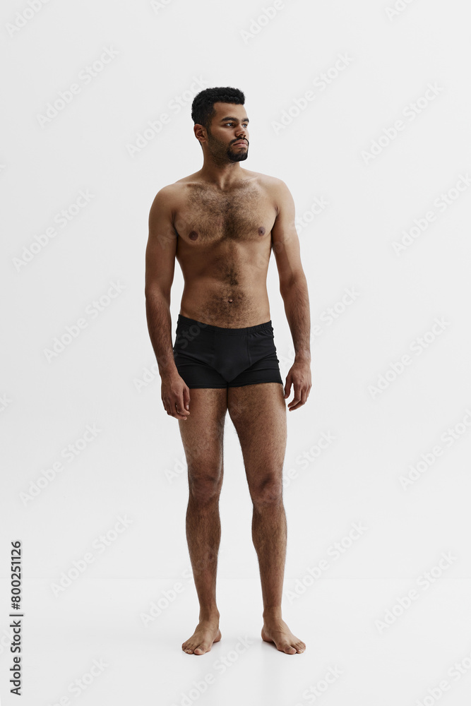 Fototapeta premium Full-length image of handsome African-American man standing shirtless in black boxes isolated on white background. Masculinity. Concept of male beauty, sport, body care, health, fitness