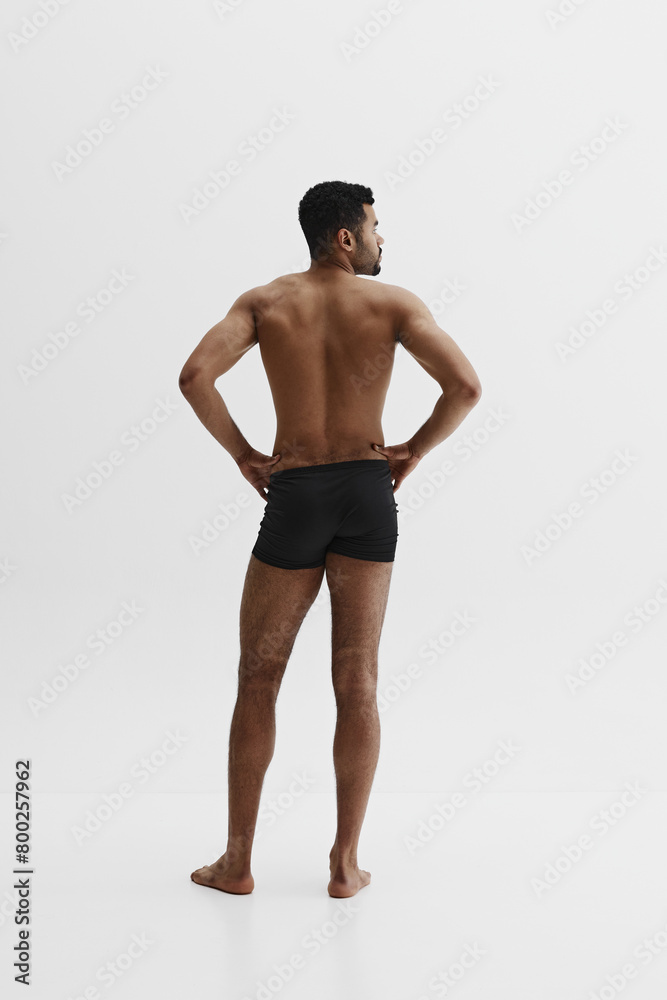 Back view. Young African-American man with relief strong back, muscular body standing in black boxers isolated on white background. Concept of male beauty, sport, body care, health, fitness