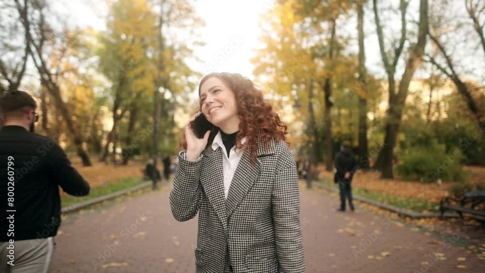 Happy young beautiful red-haired woman talking on mobile phone in autumn park. Pretty laughing girl with smartphone has a good time in autumn weekend Happy young beautiful red-haired woman talking on mobile phone in autumn park. Pretty laughing girl with smartphone has a good time in autumn weekend