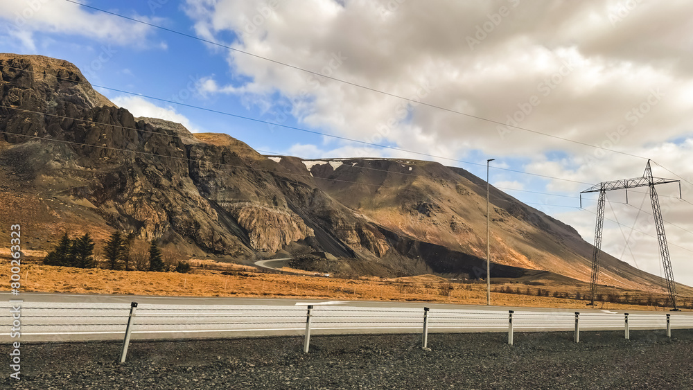 Photo of Icelandic landscapes, a high mountain along a route with power transmission. Volcanic mountains, against the backdrop of a beautiful sky with clouds. Photo of Icelandic landscapes, a high mountain along a route with power transmission. Volcanic mountains, against the backdrop of a beautiful sky with clouds.