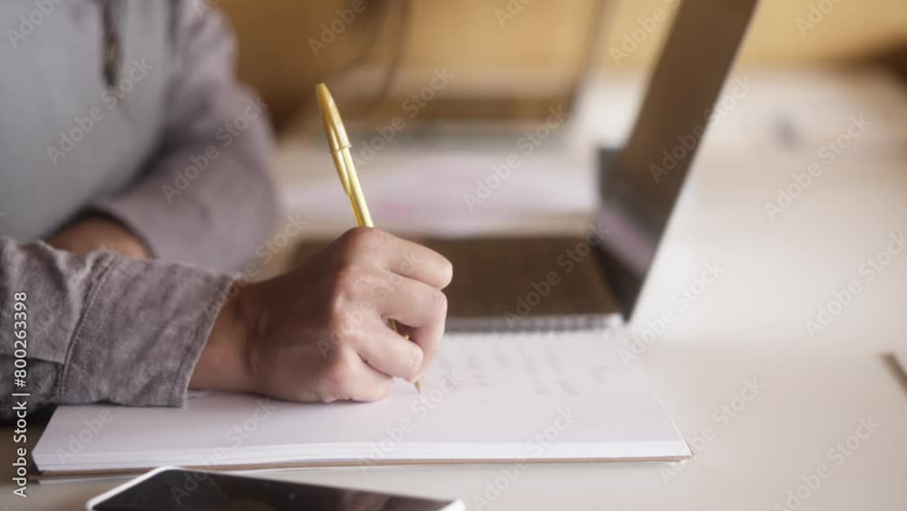 Detail of Latin business man writing in paper and typing laptop at desk. Detail of Latin business man writing in paper and typing laptop at desk.