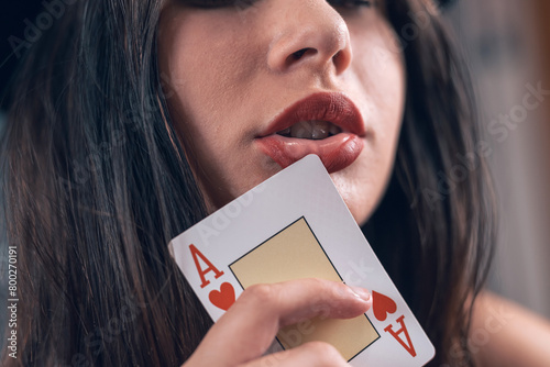 close up portrait of pretty female poker player hold ace near red lips